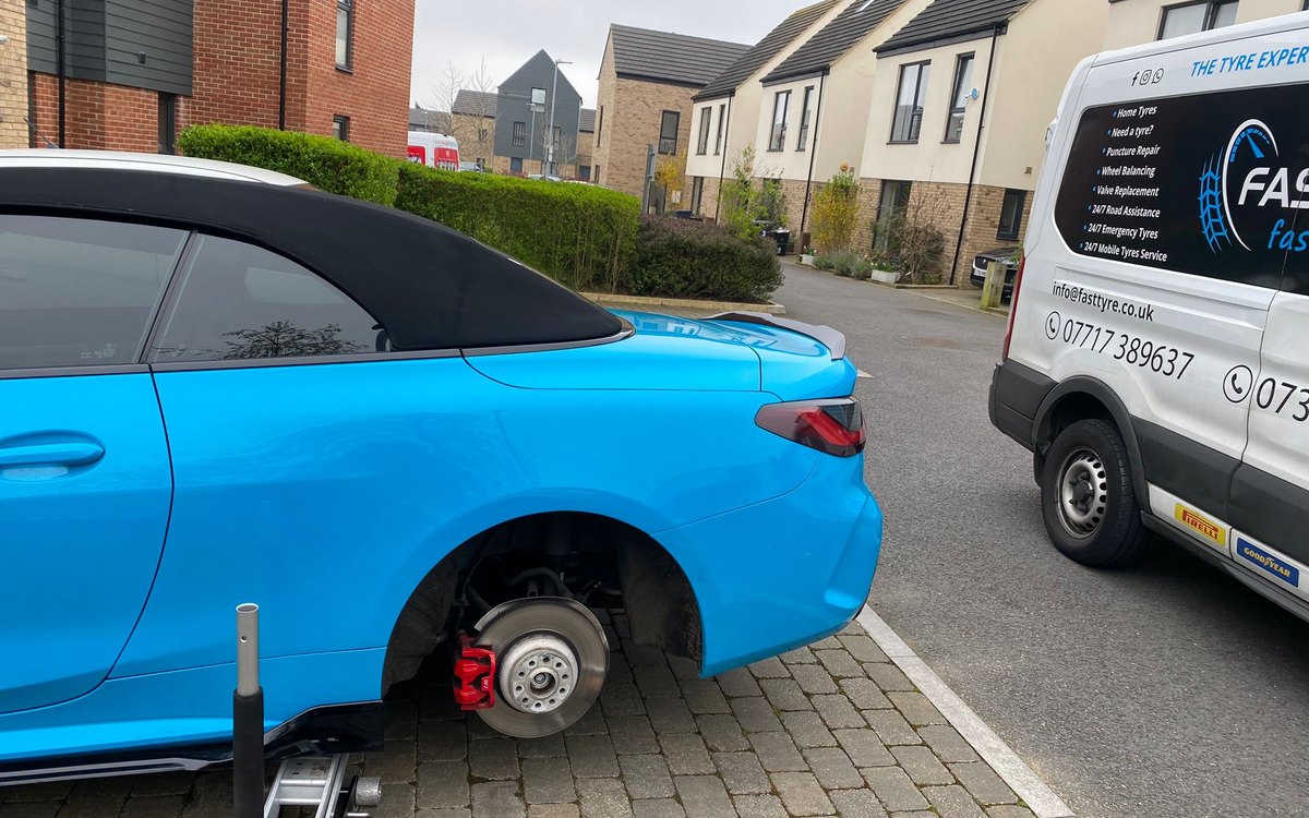 A blue BMW convertible on a driveway with its front wheel removed and a Fast Tyre van alongside