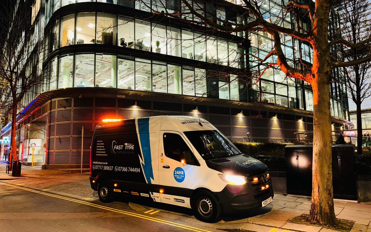 A Fast Tyre van with its beacon lit outside a lit office building in London at night