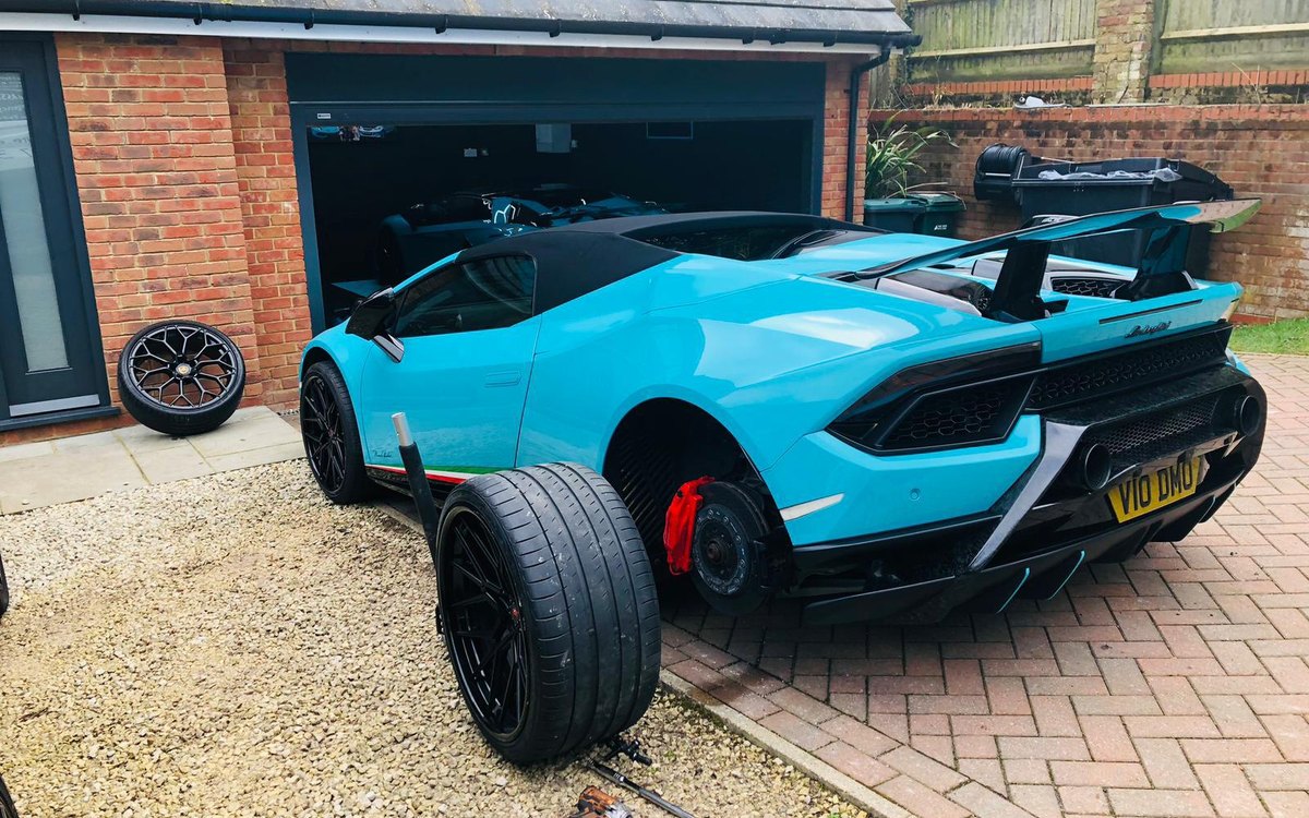 A blue Lamborghini on a driveway with its rear wheel removed and the tyre on the ground